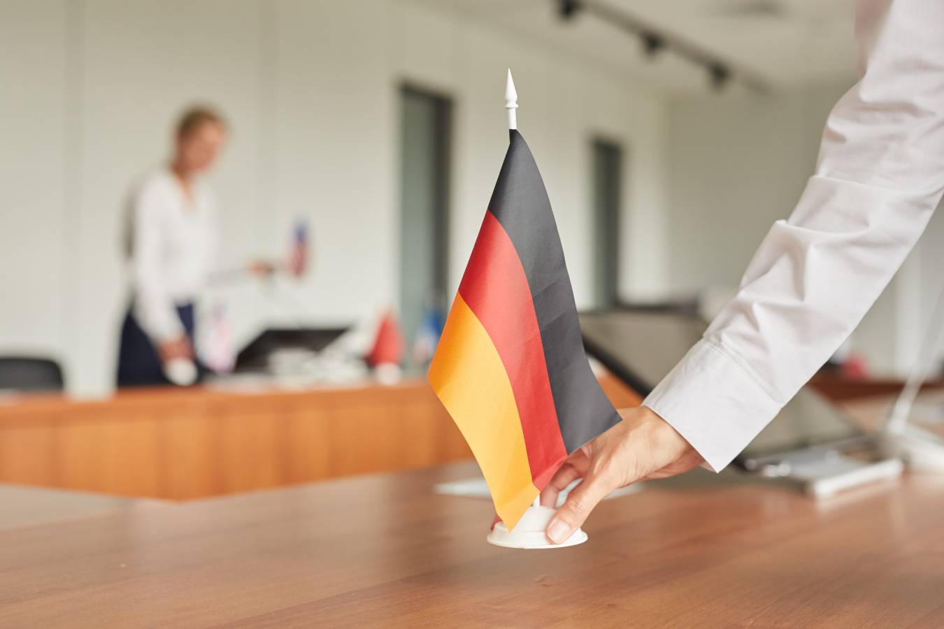close-up-female-assistant-placing-german-flag-table-while-preparing-conference-room-international-business-event.jpg